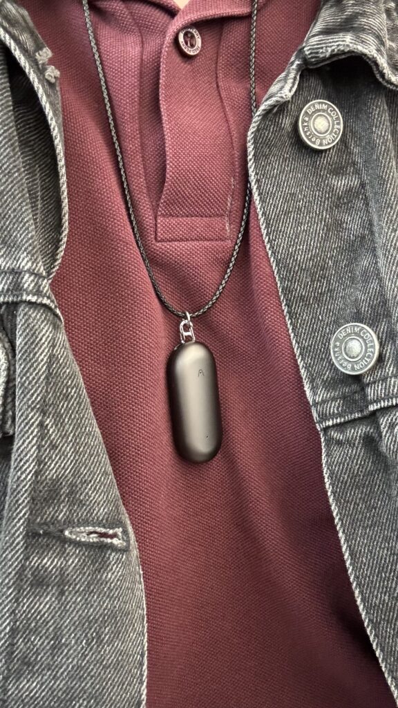 The Plaud Note Pin around the users Neck in the necklace option in grey colour.